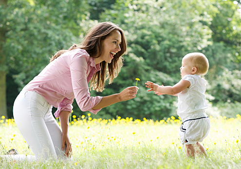 Happy mother teaching baby to walk in the park